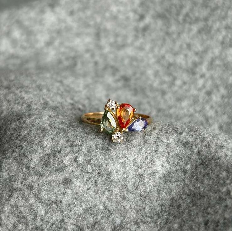 Bague en or sertie de saphirs multicolores, posée sur du feutre gris