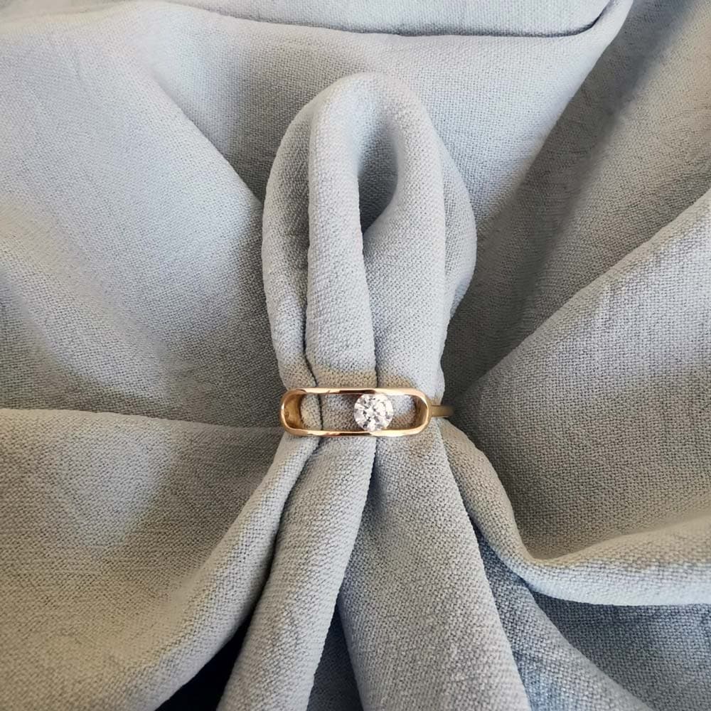 Fine bague solitaire en or posée sur un tissu gris plissé